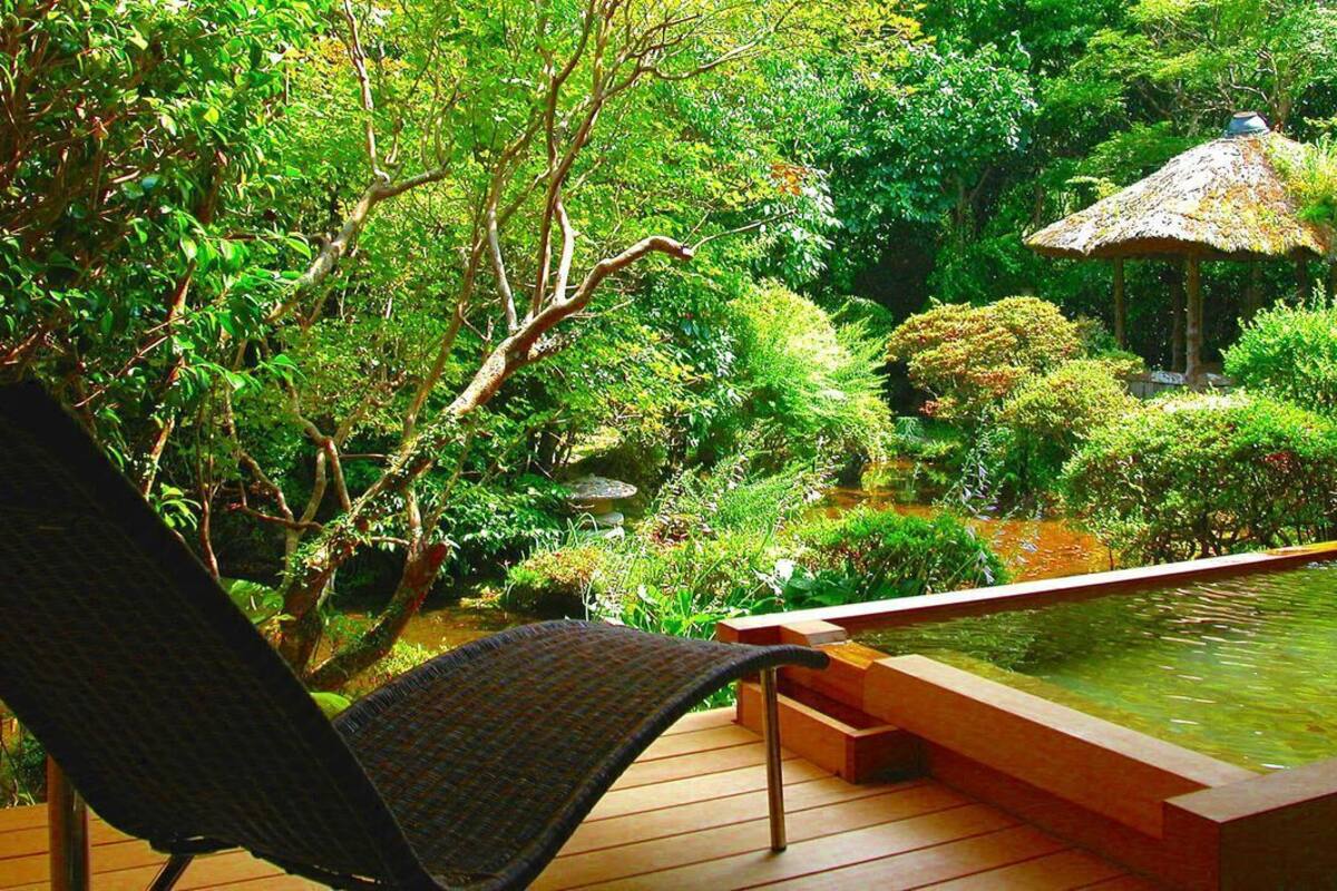 A wooden deck with a chair, a small pond, and a thatched-roof structure.
