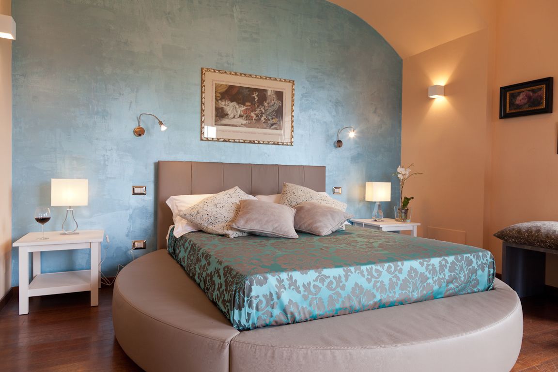 Una camera da letto con un letto grande, due comodini, un tavolino e un quadro appeso al muro, oltre a un punto luce a parete.