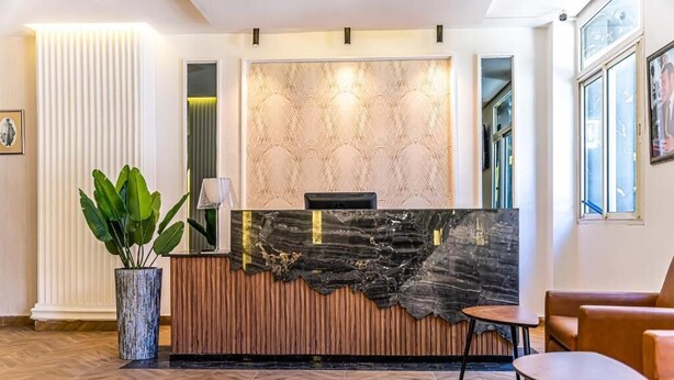 A reception area with a marble counter, a potted plant, and a seating area with two chairs and a table. - Hotel Les Ambassadeurs (Casablanca)