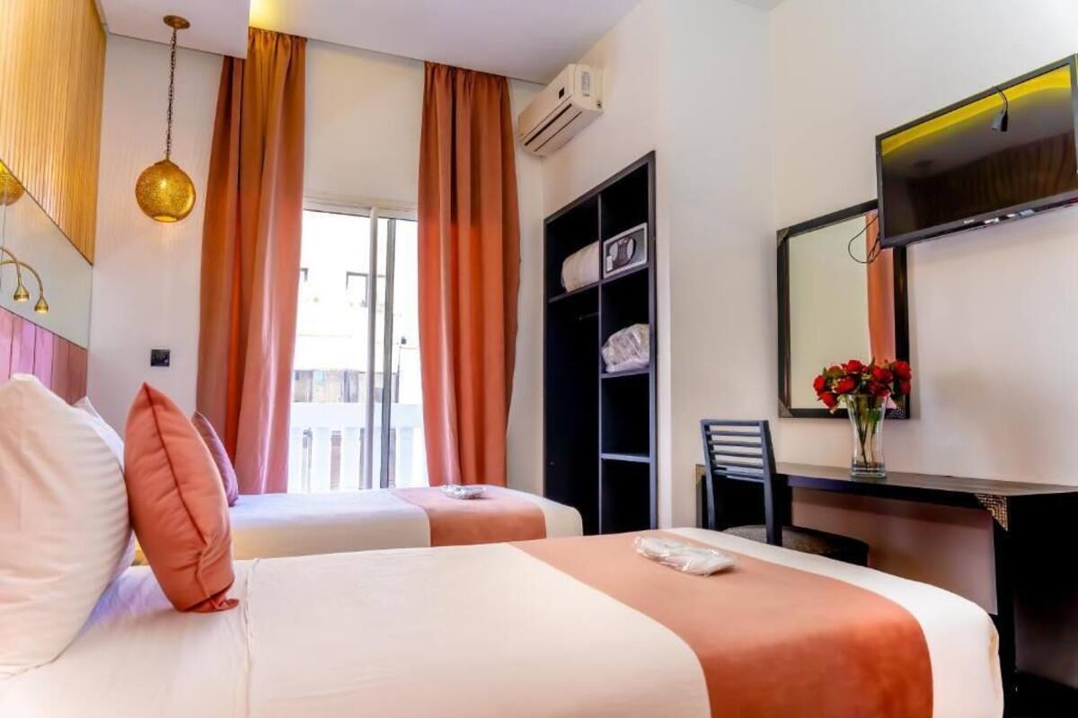 Habitación de hotel con dos camas, un escritorio, una silla, un espejo y una ventana con cortinas.