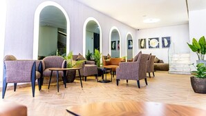 A modern lounge area with multiple seating options, including sofas and armchairs, arranged around a central coffee table. There are several potted plants adding greenery to the space. - Hotel Les Ambassadeurs (Casablanca)