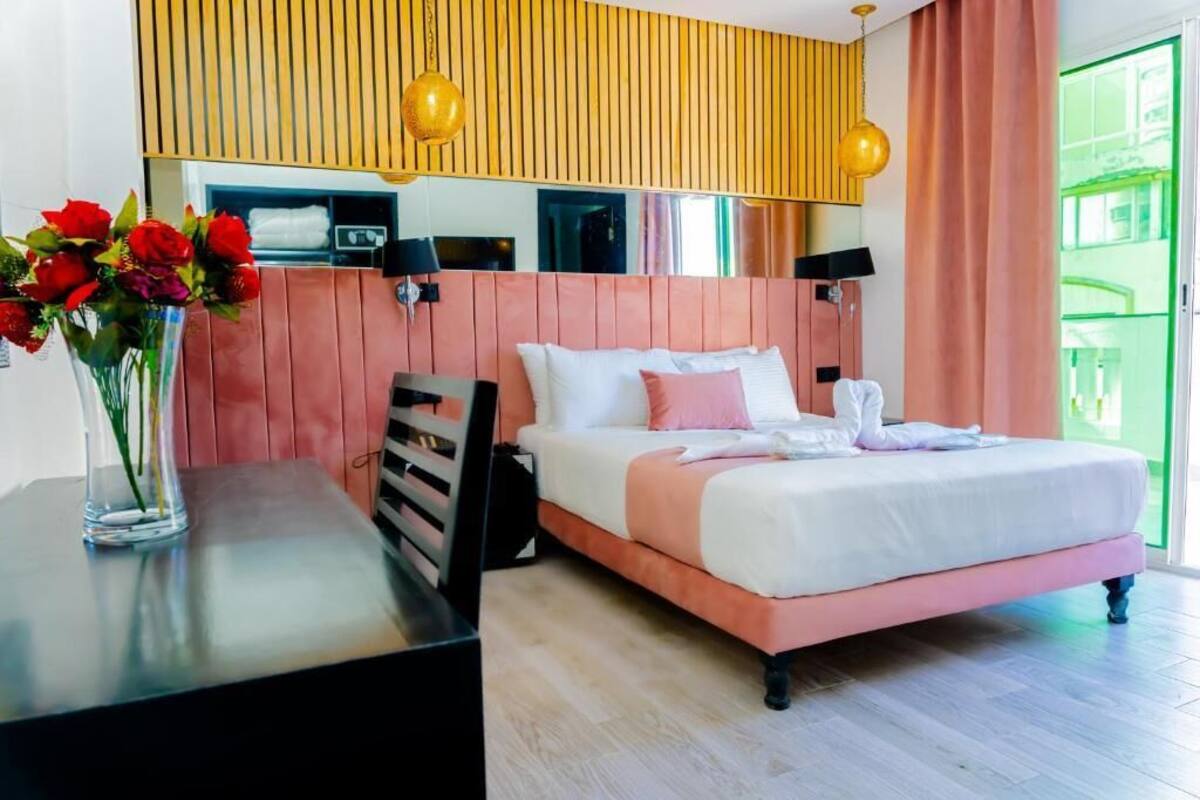 Habitación de hotel moderna con cama, escritorio, un florero y vista a un área verde al aire libre.