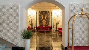 Un hall con suelo de mármol, sofás rojos, una gran obra de arte en la pared y una silla dorada.