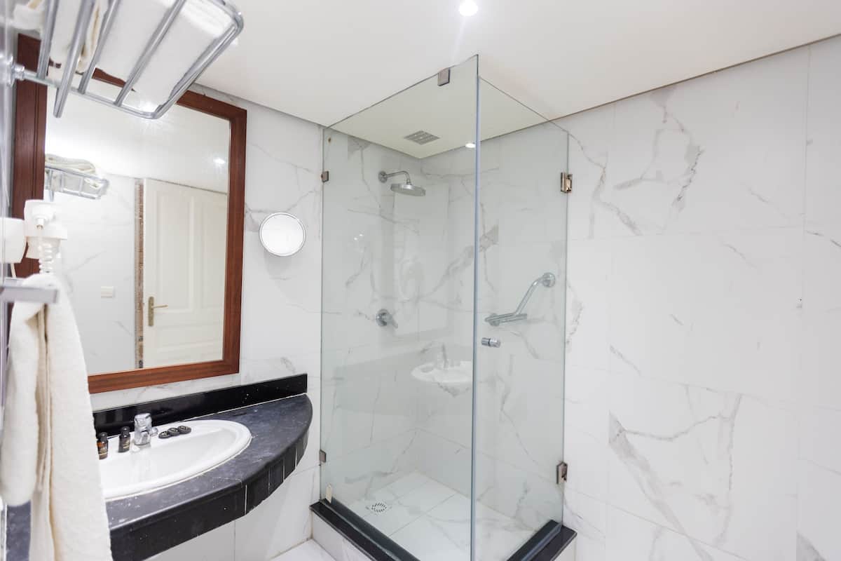A modern bathroom with a glass-enclosed shower, a sink with a marble countertop, and a large mirror.