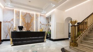 Un vestíbulo con mostrador de recepción, una escalera con barandillas ornamentadas y un muro con diseño.