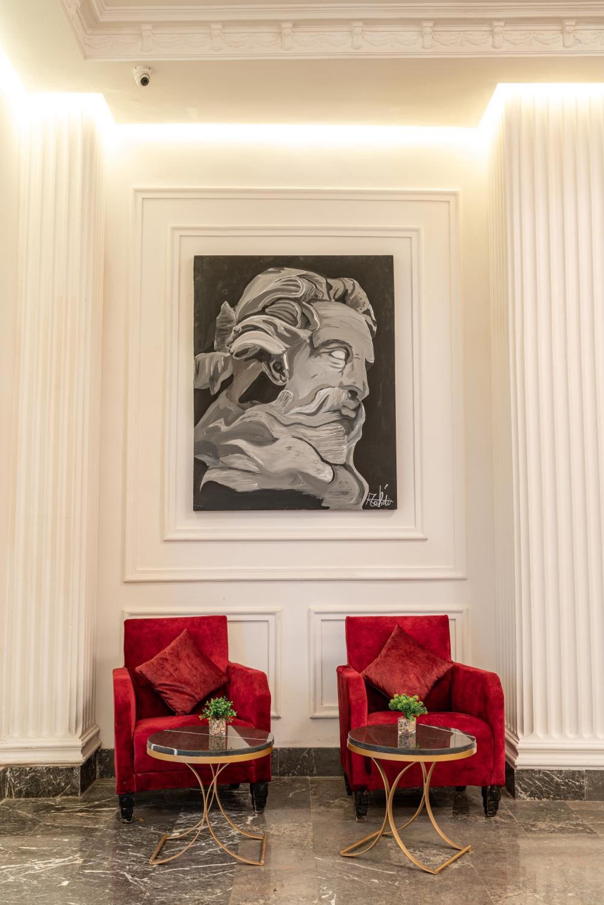 A lobby with two red velvet armchairs, a marble floor, and a large framed artwork on the wall.