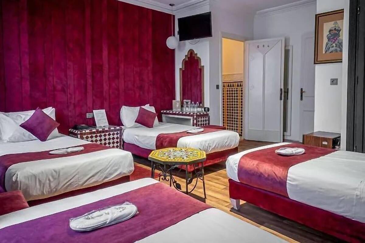 A hotel room with three beds, a television, a small table, and a door leading to another room.