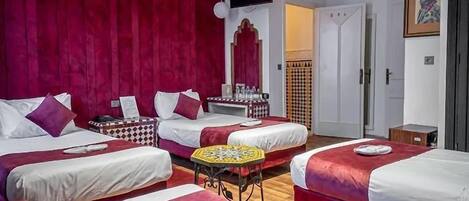 A hotel room with three beds, a television, a small table, and a door leading to another room.
