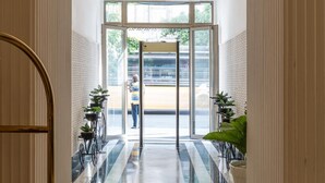 Un vestíbulo de hotel con piso de mármol, una escalera central y un amplio ventanal que da al exterior.