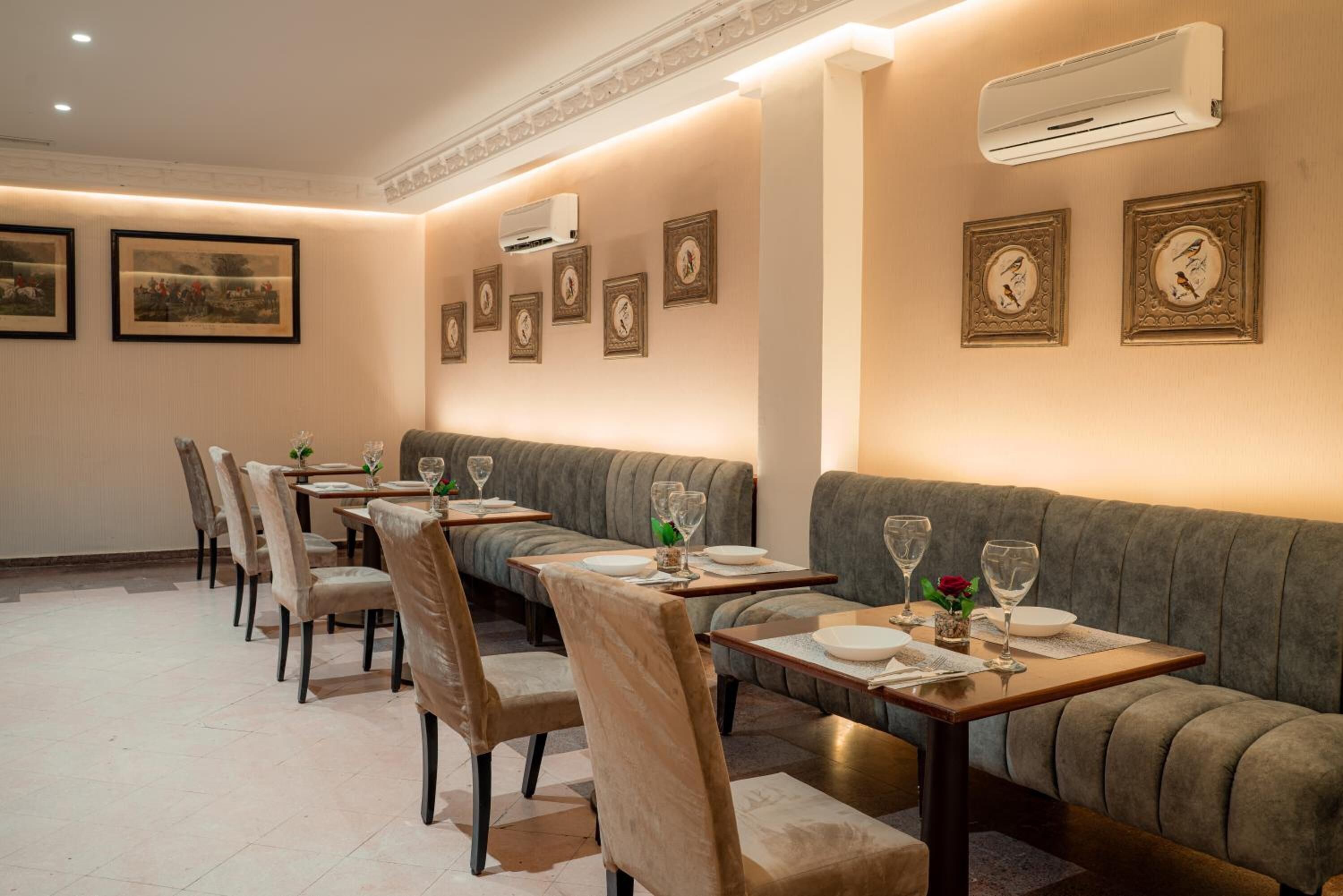 A dining area with tables set for two, cushioned seating, and framed artwork on the walls.