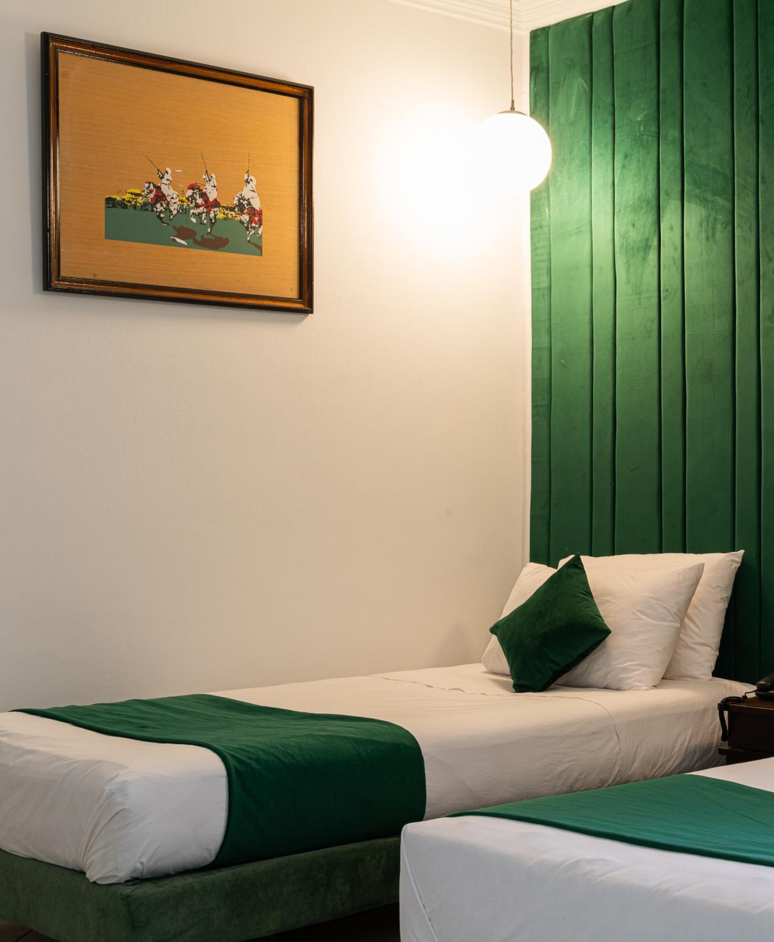 Een hotelkamer met twee bedden, een groen hoofdeinde, een ingelijste foto aan de muur en een bedlampje.