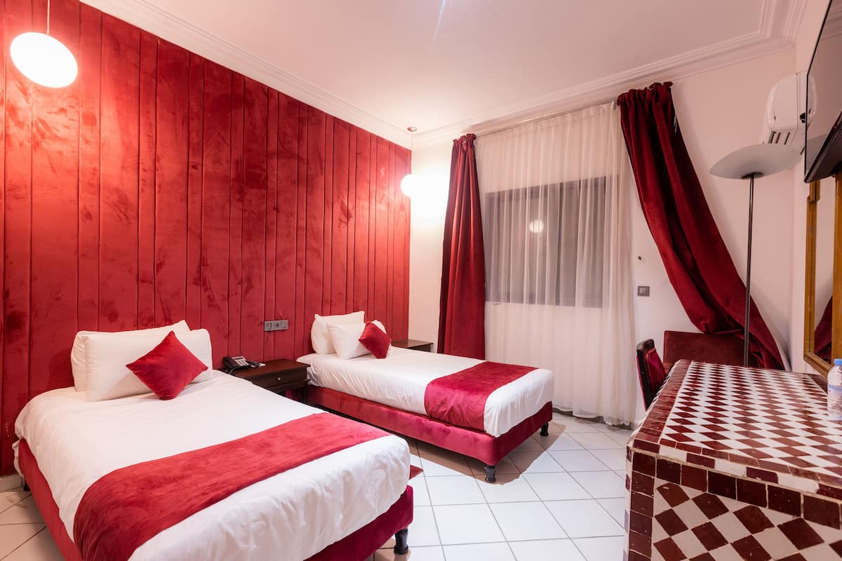 A hotel room with two beds, a checkered table, a red curtain, and a white ceiling.