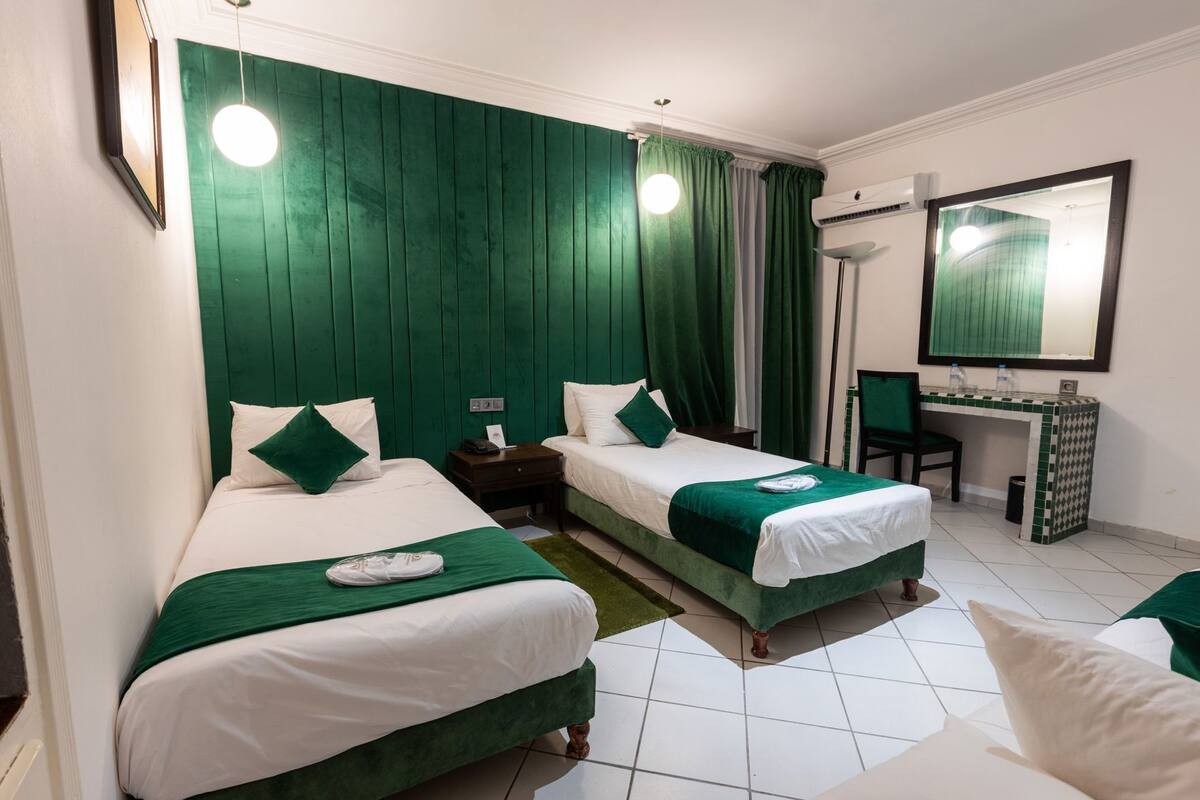 A hotel room with two beds, a desk, a chair, and a mirror.