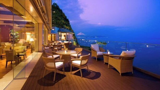 A deck with wicker furniture and a view of a mountain and cityscape. - Yaizu Grand Hotel (Shizuoka)