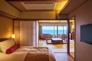 Un cuarto de hotel con cama, televisión y vista al mar a través de amplias ventanas.