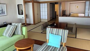 A traditional Japanese-style room with tatami flooring, a green sofa, a striped chair, and a wooden table. - Yaizu Grand Hotel (Shizuoka)