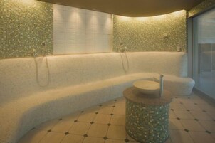 Un área de spa con un banco curvo, una pared con mosaicos y una pequeña mesa redonda con un taburete.