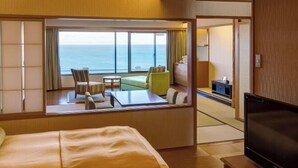 A hotel room with a large bed, a TV, a seating area with a view of the sea, and a small desk. - Yaizu Grand Hotel (Shizuoka)
