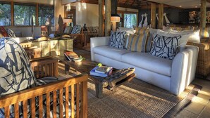 A spacious living area with a white sofa, wooden furniture, and a thatched roof ceiling.