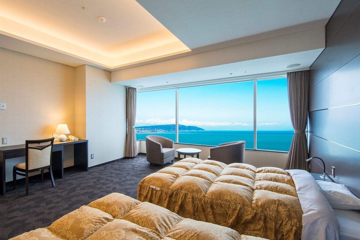 Ein Hotelzimmer mit einem großen Bett, einem Schreibtisch mit Stuhl, einem kleinen Tisch und Blick aufs Meer.