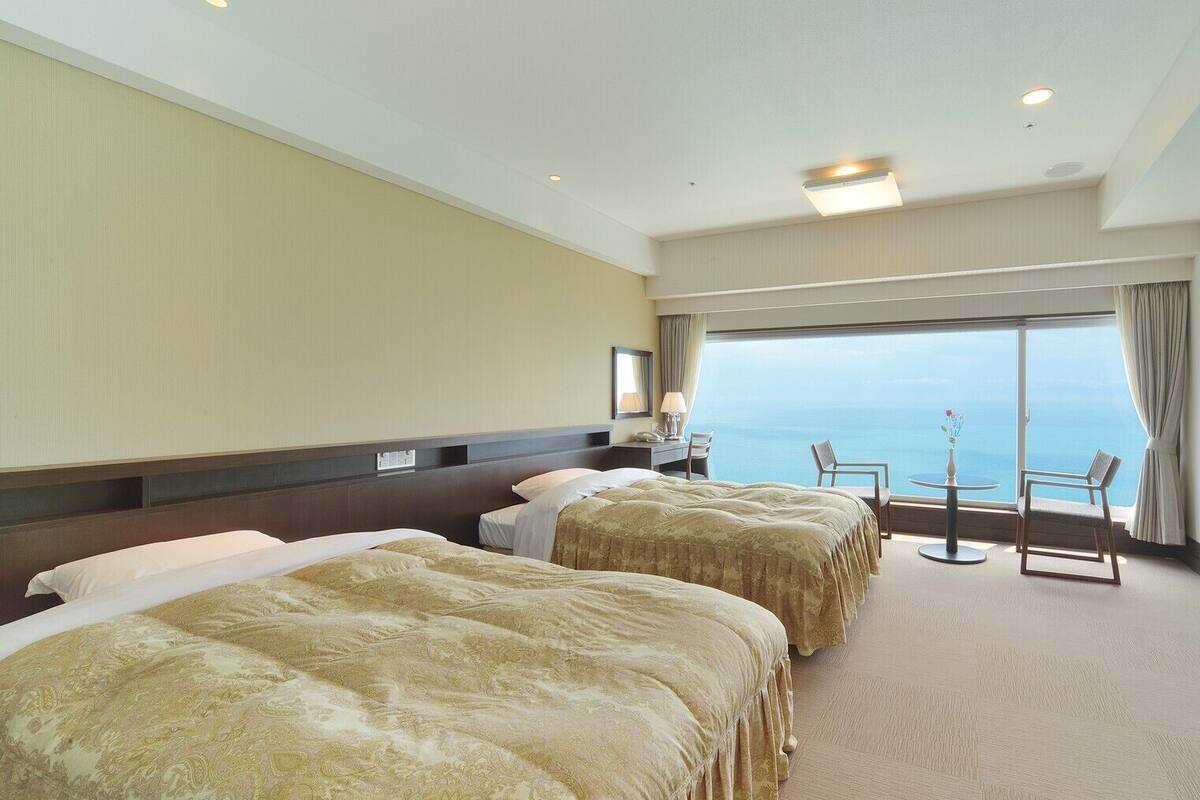 Ein Hotelzimmer mit zwei Betten, einem Schreibtisch, einem Stuhl, einem kleinen Tisch und einem Fernseher.