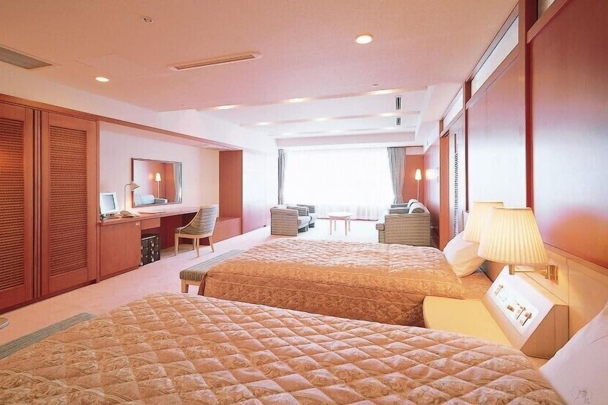 Une chambre d’hôtel avec deux lits, un bureau, une chaise, un miroir et une vue sur l’extérieur.
