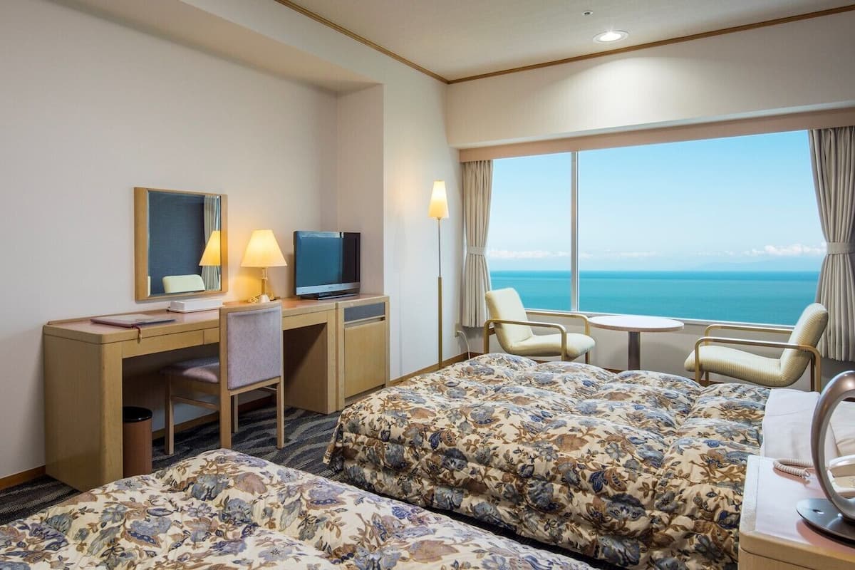 Ein Hotelzimmer mit Bett, Schreibtisch mit Computer, Stuhl, kleinem Tisch und Meerblick.