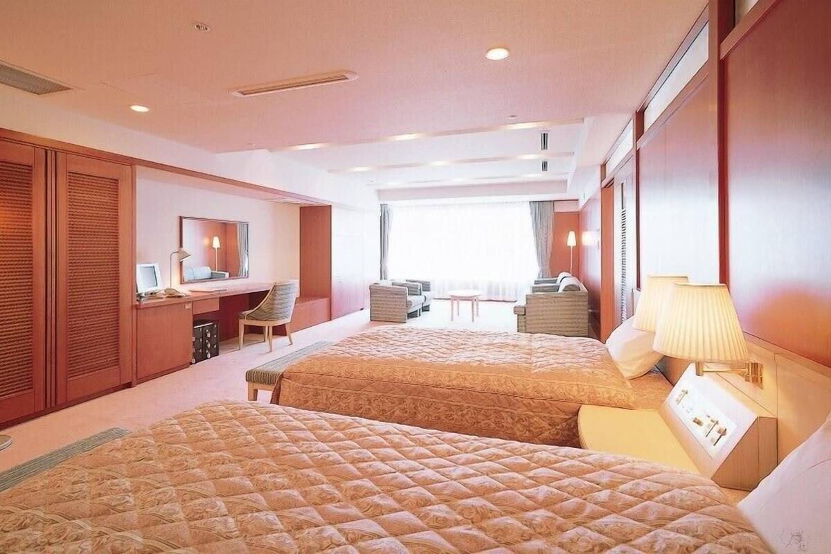 Ein Hotelzimmer mit zwei Betten, einem Schreibtisch, einem Sessel, einer Couch und einem großen Fenster.