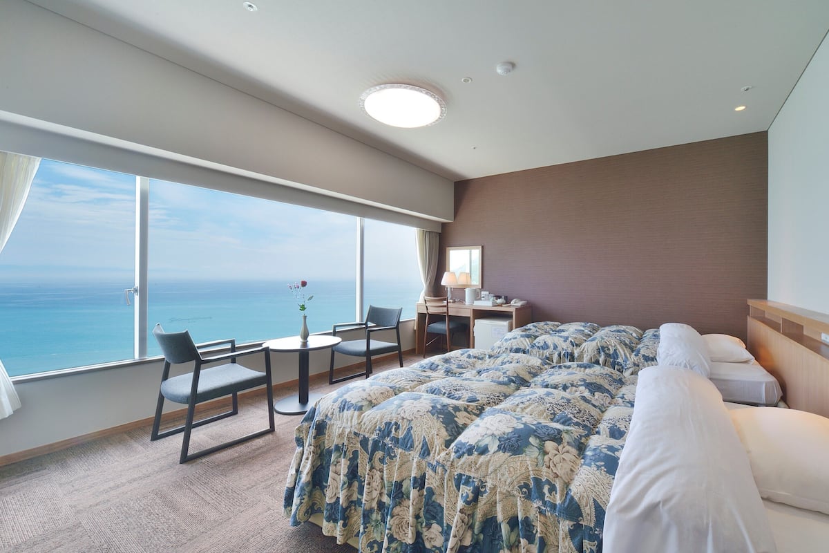 Ein Hotelzimmer mit einem großen Bett, einem Schreibtisch mit Stuhl, einem kleinen Tisch und Blick auf den Ozean.