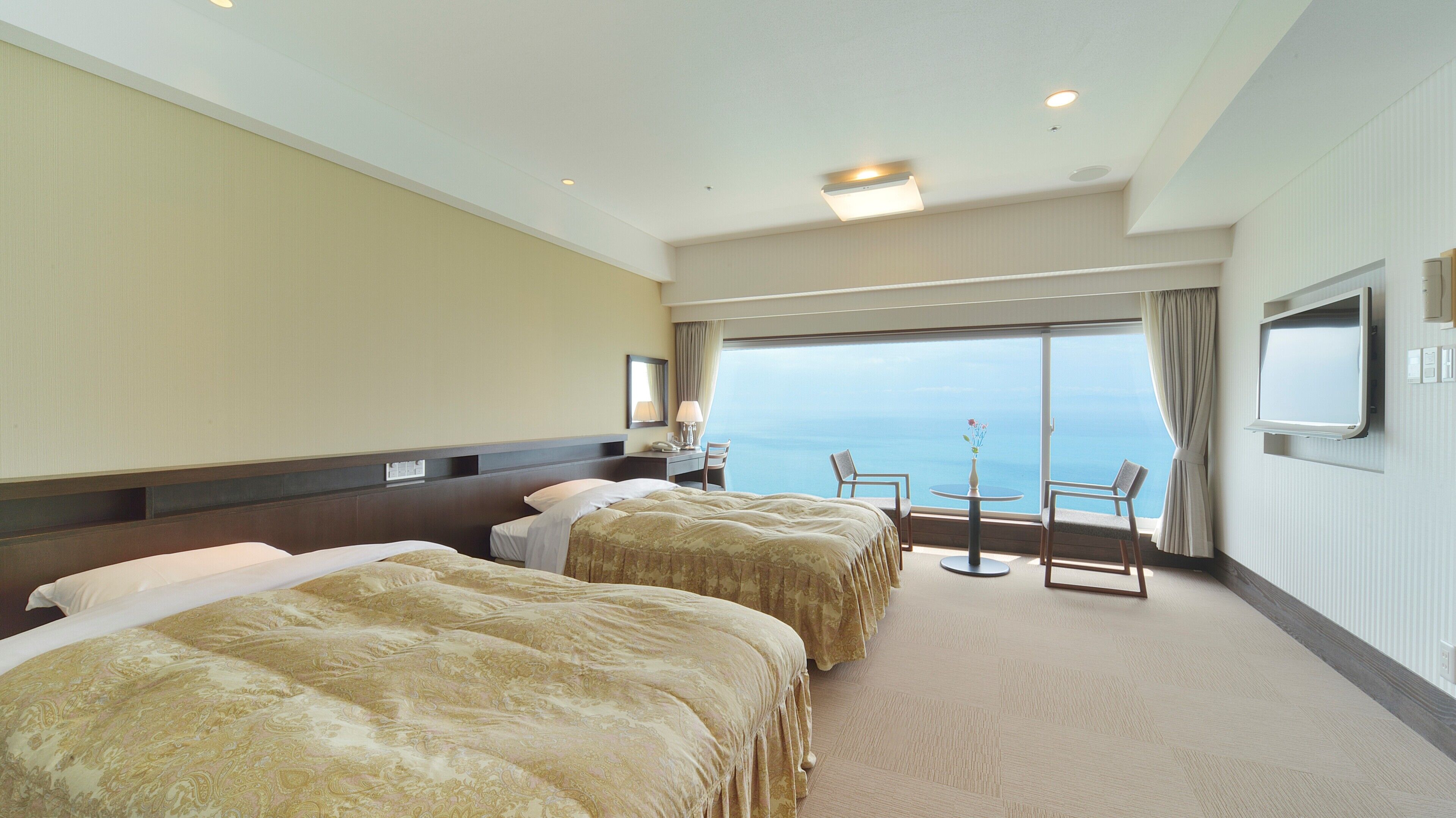 Ein Hotelzimmer mit zwei Betten, einem Schreibtisch, einem Sessel, einem Fernseher und Meerblick.