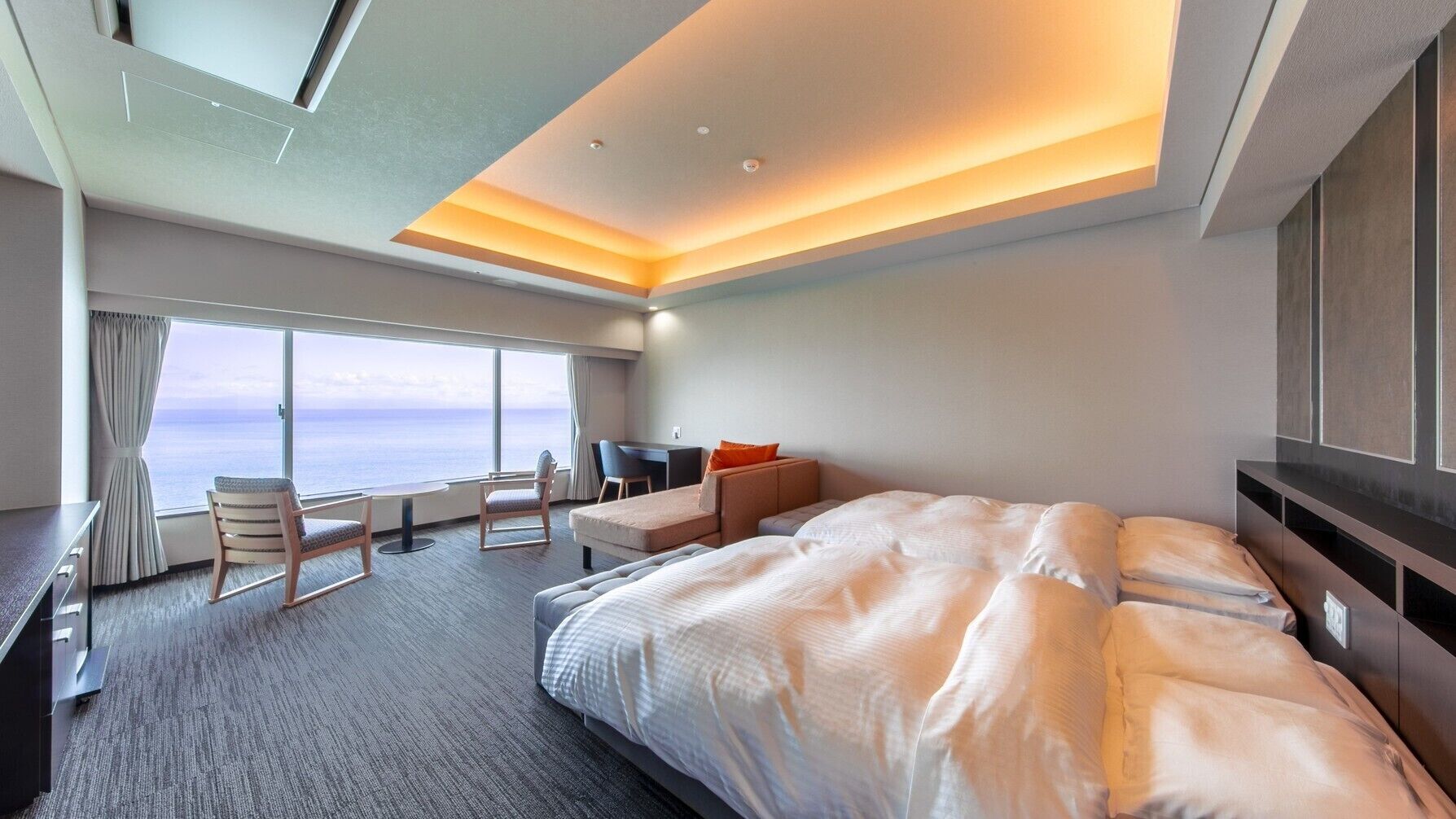 Ein modernes Hotelzimmer mit einem großen Bett, einem Schreibtisch, einem Sessel und Blick aufs Meer.