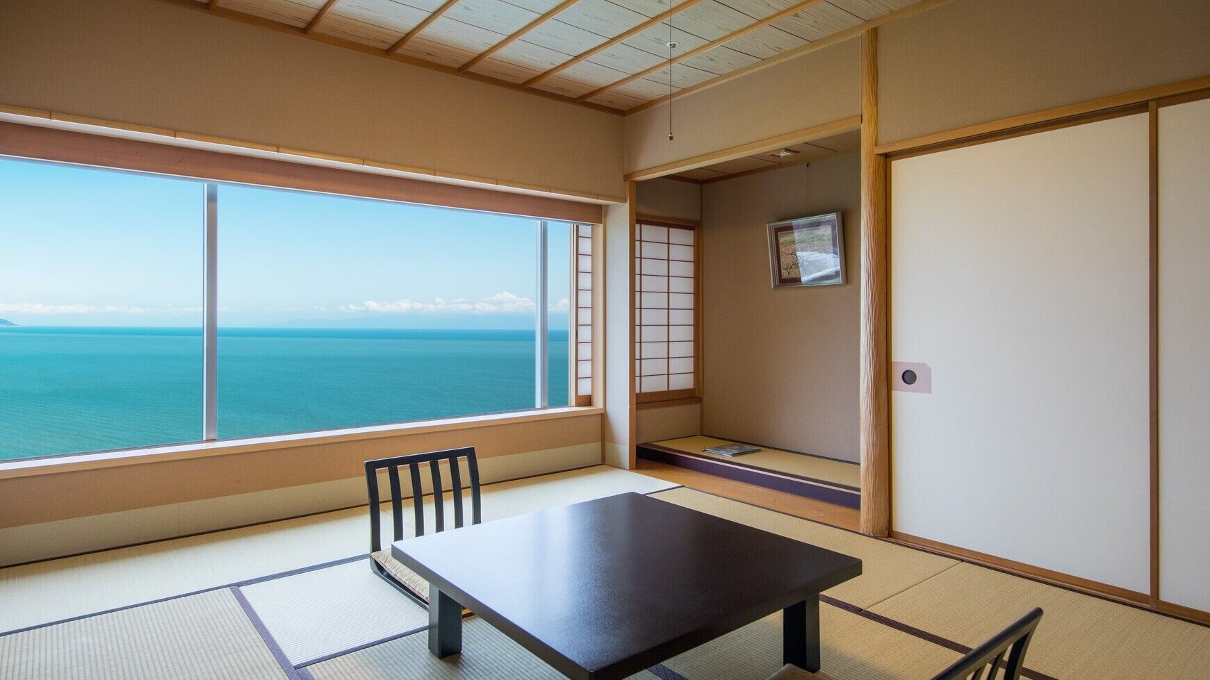 Ein Zimmer mit Tatami-Boden, einem niedrigen Tisch, einem Stuhl, einer Schiebetür und Meerblick.