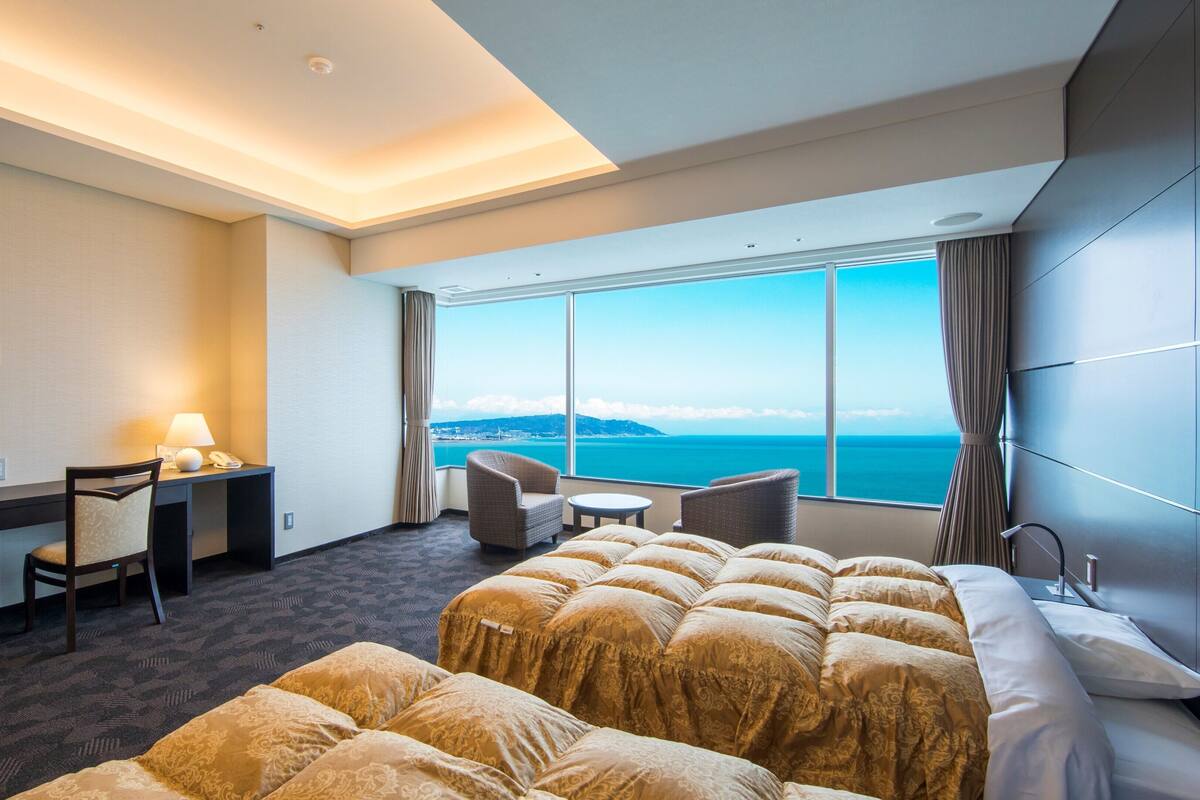 Ein Hotelzimmer mit Bett, Schreibtisch mit Lampe, Stuhl, kleinem Tisch und Meerblick.