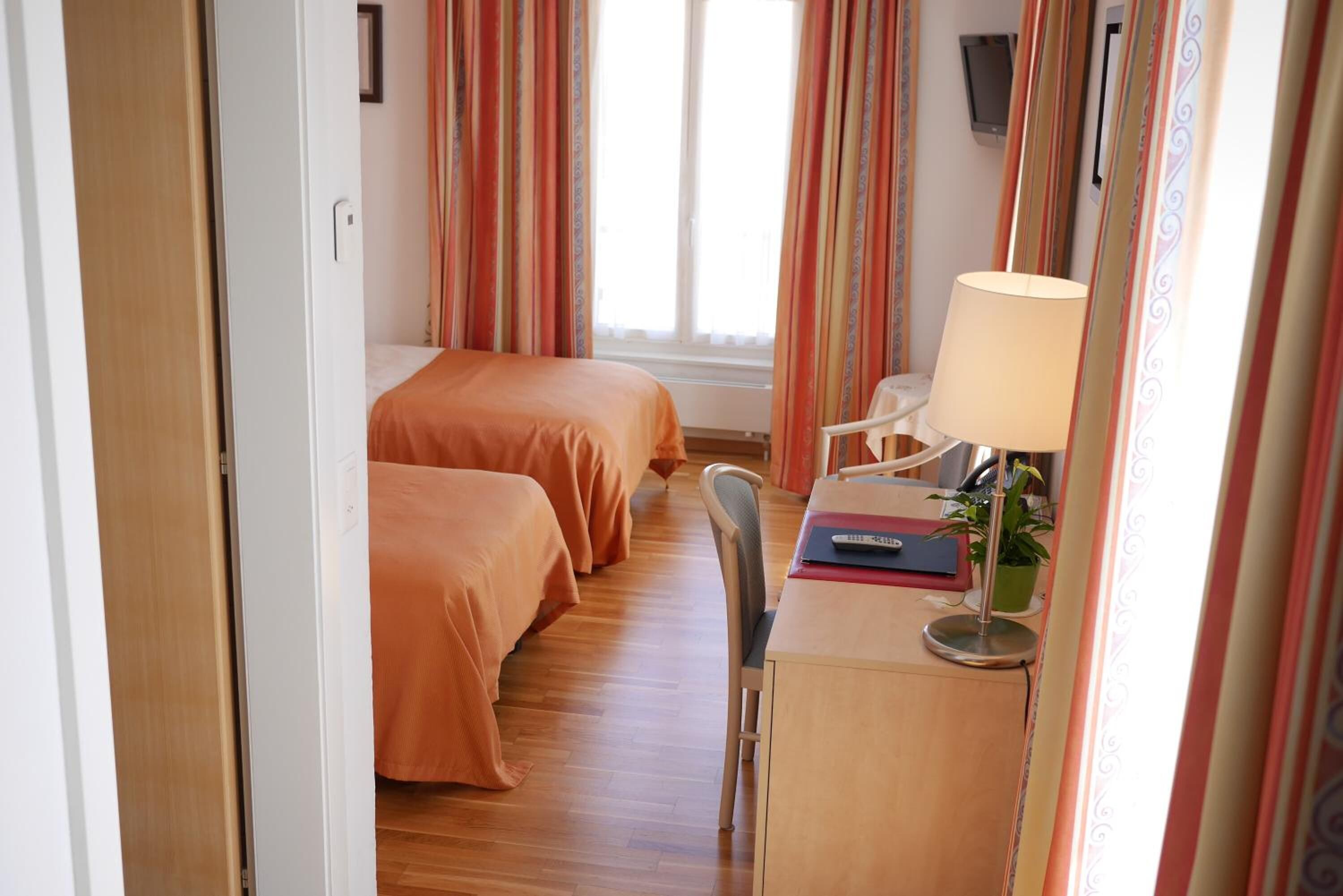 Een hotelkamer met twee bedden, een bureau met lamp, een stoel en een potplant.