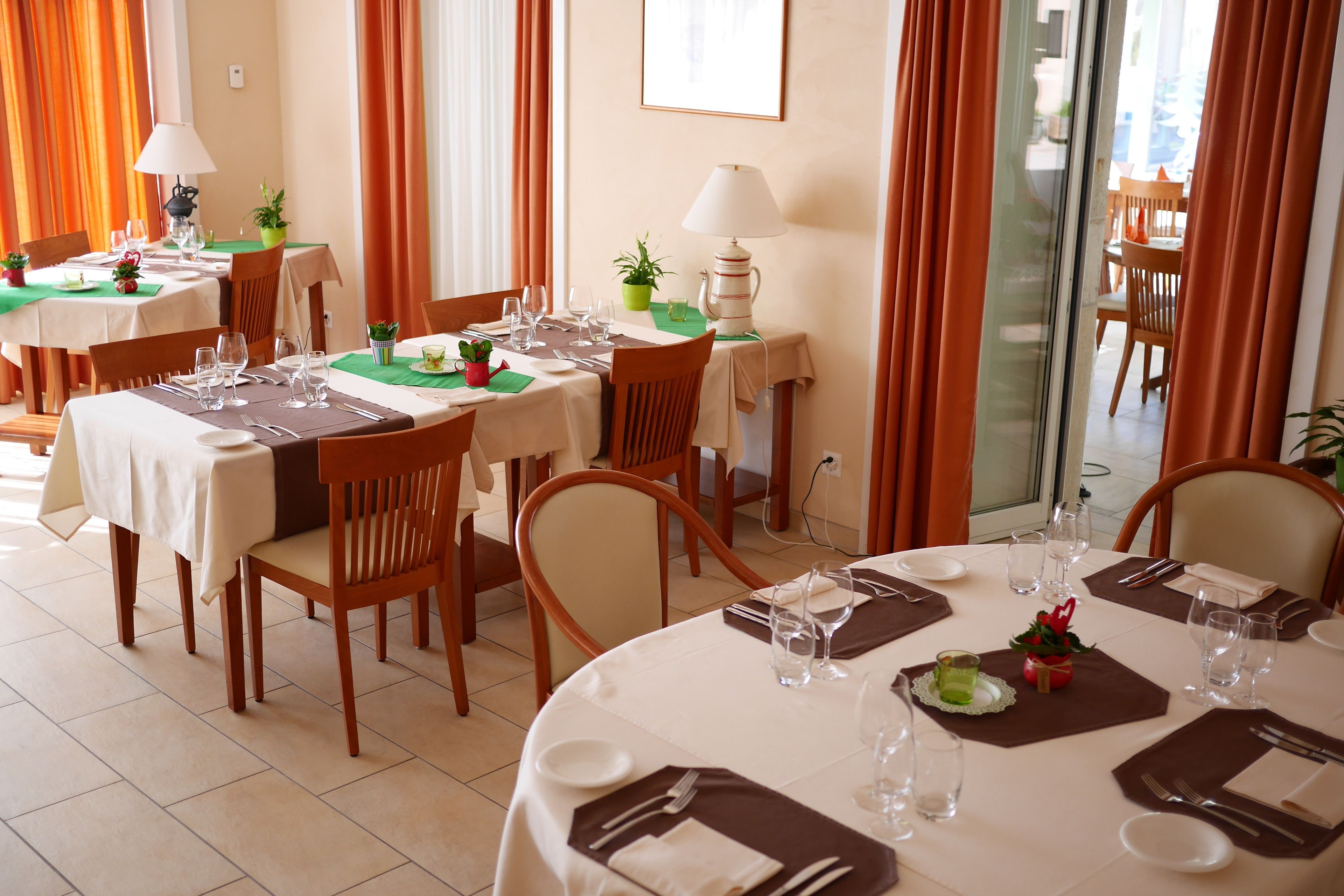 A dining area with multiple tables set for guests, each with a tablecloth, placemats, and neatly arranged cutlery.
