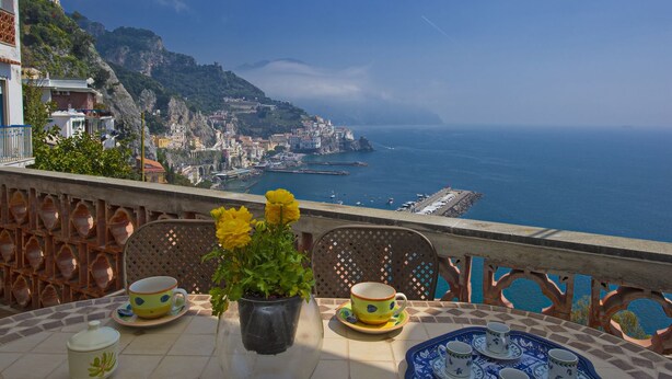 Una terraza con una mesa preparada para tomar té, con vistas a un pueblo costero y al mar.