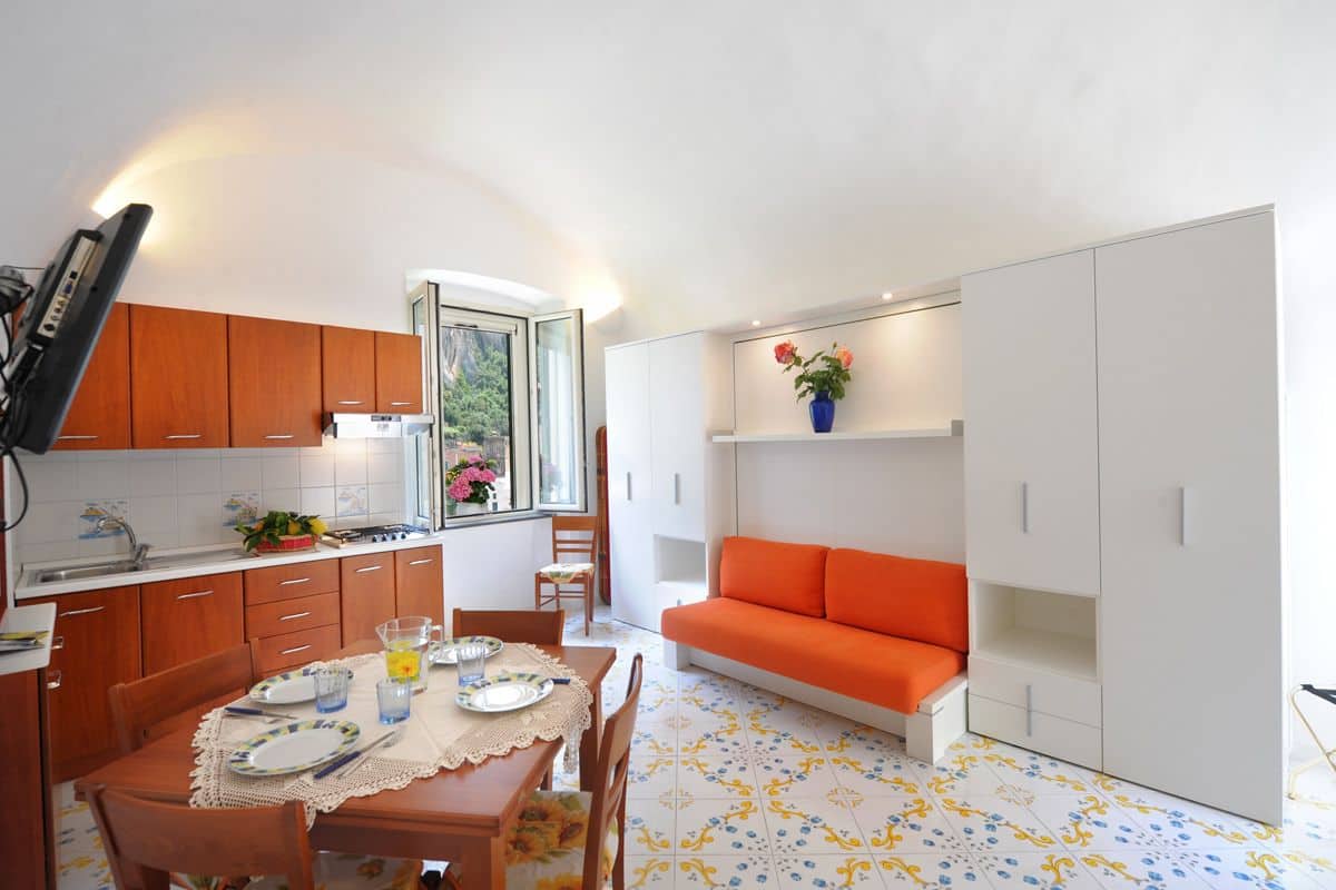 Una cocina compacta con armarios de madera, una mesa de comedor dispuesta con platos y cubiertos, y una ventana con vistas a zonas verdes.
