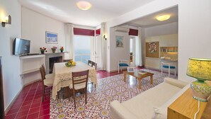 Un comedor con una mesa dispuesta para dos, un televisor montado en la pared y vista al mar desde la ventana.