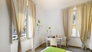 Una habitación de hotel con una cama, una mesa de comedor con sillas y cortinas en las ventanas.