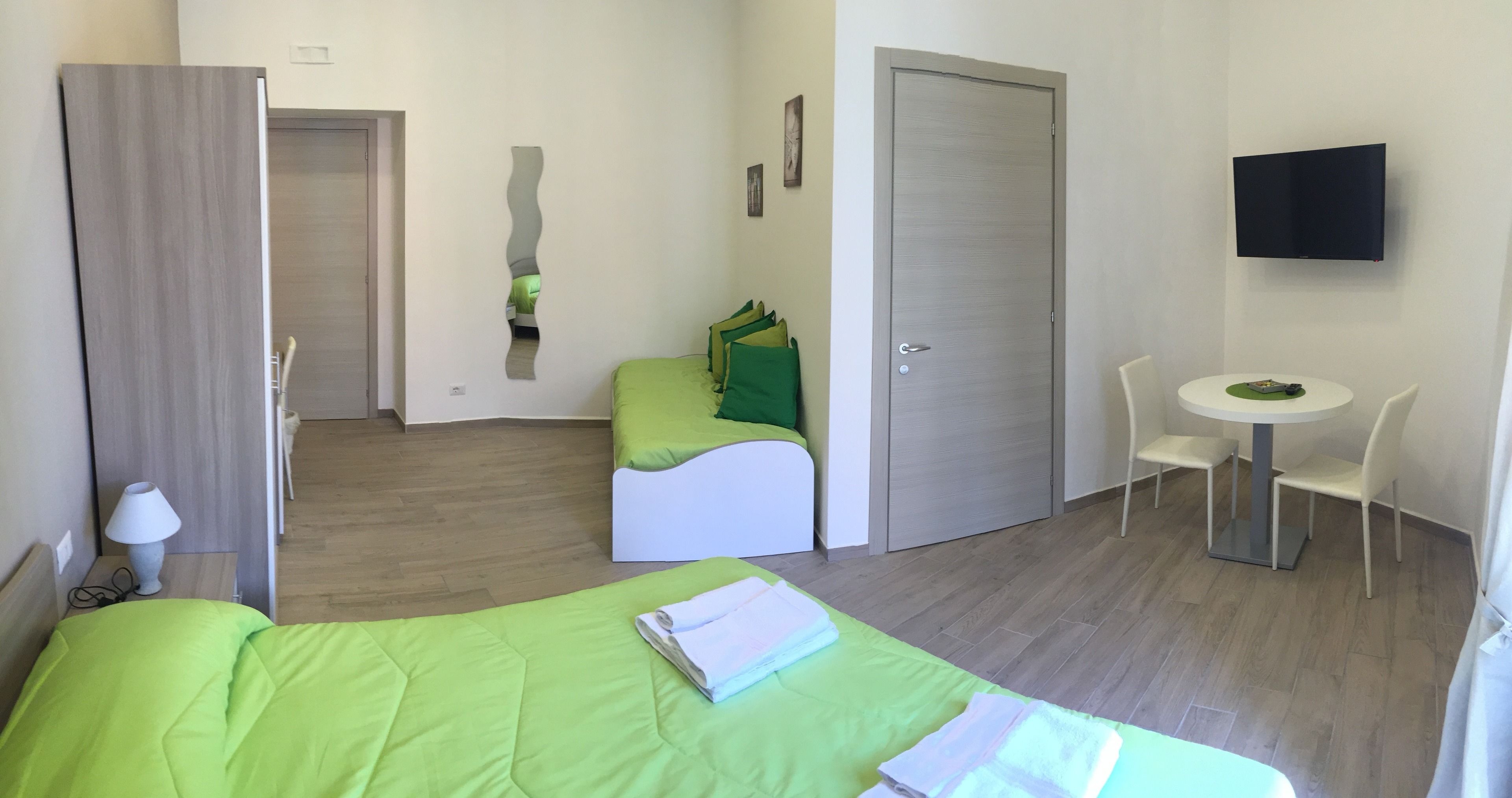 Quarto de hotel com uma cama, um pequeno espaço de estar, uma mesa e uma televisão.