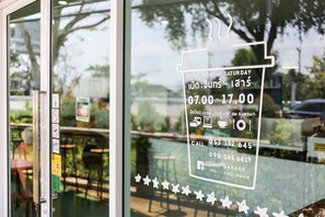 A restaurant window with a sign indicating it is open Monday to Saturday from 7:00 to 17:00, closed on Sundays, and includes contact numbers and social media handles.