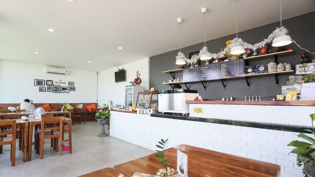 Un restaurant avec des tables et des chaises en bois, un comptoir où est affiché le menu, et un téléviseur fixé au mur.