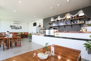 Un restaurant avec des tables et des chaises en bois, un comptoir où est affiché le menu, et un téléviseur fixé au mur.