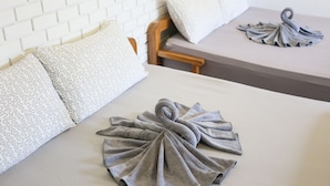Une chambre d’hôtel avec un mur en briques blanches, une tête de lit en bois et deux lits sur lesquels sont disposées deux serviettes grises, formant la silhouette d’un cygne.