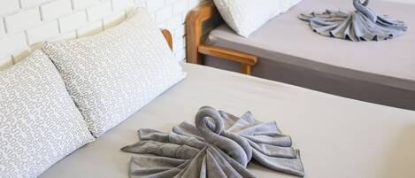 Habitación de hotel con pared de ladrillo blanco, cabecera de madera y dos camas con toallas grises dispuestas en forma de cisne.