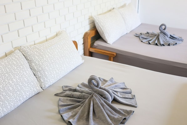 Habitación de hotel con pared de ladrillo blanco, cabecera de madera y dos camas con toallas grises dispuestas en forma de cisne.