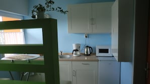 A kitchen with white cabinets, a microwave, a coffee maker, and a plant on the window sill. - Gästezimmer Vogelsberg (Freiensteinau)