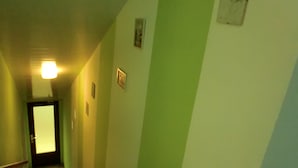 A narrow hallway with a door at the end, a light fixture on the ceiling, and a wall with a green stripe. - Gästezimmer Vogelsberg (Freiensteinau)