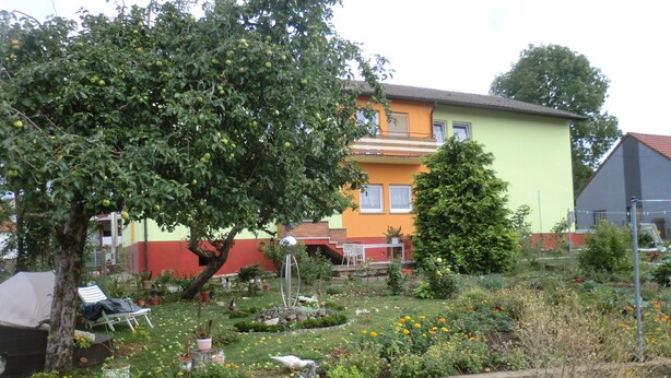 A garden with a lawn, a tree, and a building with a balcony. - Gästezimmer Vogelsberg (Freiensteinau)