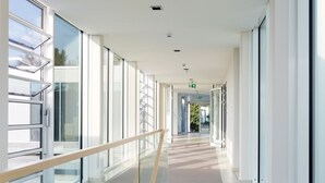 A modern interior with a glass railing, a staircase, and large windows. - Strandhotel Senftenberger See (Senftenberg)